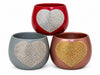 Shot of three large ceramic planters in red, grey and pink. All pots have a large crystal heart on the front. 