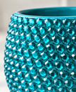A close-up of a turquoise blue ceramic planter covered in faceted, jewel-like round crystals, with a soft blurred neutral background.