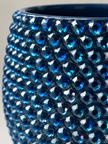 Close-up of a glossy navy textured ceramic plant pot covered in faceted navy blue crystals, with a dark blue interior visible at the top against a light neutral background.
