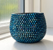 A small round decorative ceramic plant pot covered in shimmering blue and navy crystals, placed on a windowsill with natural light.