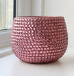 A round, dusty rose pink beaded ceramic planter, covered in small, reflective pink crystals, sitting on a white windowsill.