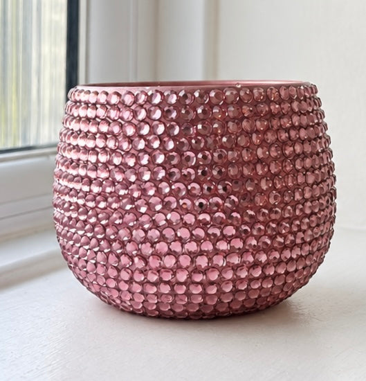 A round, dusty rose pink beaded ceramic planter, covered in small, reflective pink crystals, sitting on a white windowsill.