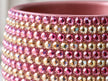 Close-up of a pink cylindrical plant pot covered with rows of faceted crystals in pink, champagne, and iridescent tones.