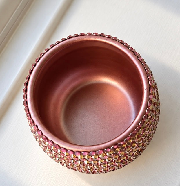 A round metallic rose gold ceramic plant pot with a textured, beaded outer rim, photographed from a top-down angle on a light off-white surface.