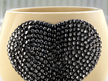 A close-up of a cream-colored ceramic  planter decorated with a large grey heart-shaped embellishment covered in faceted grey rhinestones.