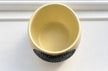 A pale Ivory ceramic plant pot with a textured grey crystal heart in its centre, shown from a top-down perspective on a white paneled surface.