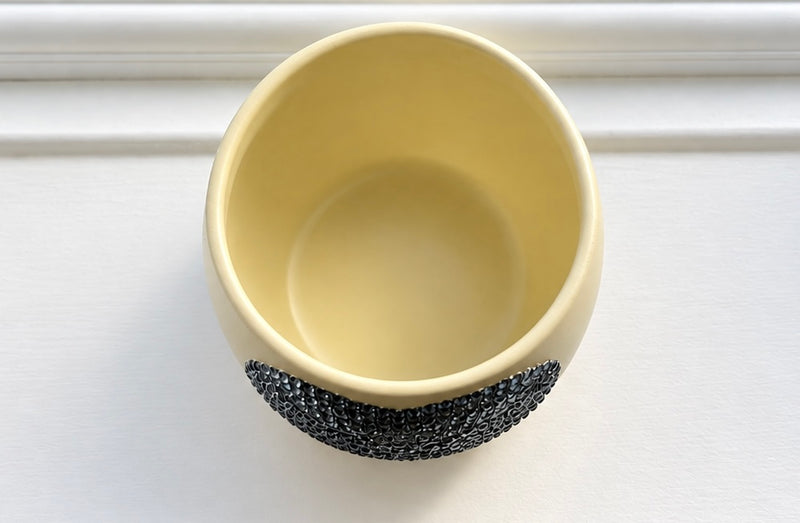 A pale Ivory ceramic plant pot with a textured grey crystal heart in its centre, shown from a top-down perspective on a white paneled surface.