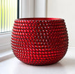 A round, glossy cerramic planter  covered in rows of faceted red crystals, set on a white windowsill with a window and white wall in the background.