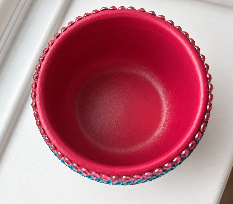 A top-down view of a round, deep plant pot with a glossy hot pink interior and a beaded rim featuring alternating pink and blue crystals, set against a white background.