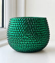 A round green ceramic planter covered in a textured, beaded pattern of faceted green stones, sitting on a white windowsill.