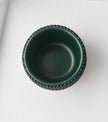 A dark green ceramic plant pot with a textured, beaded outer rim, shown from a top-down perspective on a clean white surface.