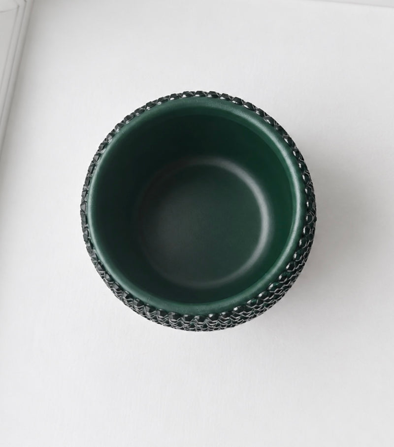 A dark green ceramic plant pot with a textured, beaded outer rim, shown from a top-down perspective on a clean white surface.