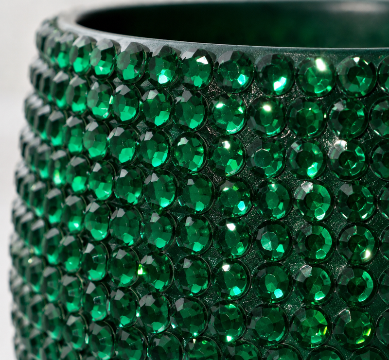 A close-up of a green ceramic plant pot  covered in faceted green crystals, showing the reflective green gems set in a dark base against a light background.