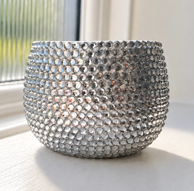 A clear crystal clear planter with a rounded, textured dome shape, shown on a light surface near a window.