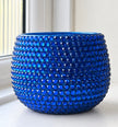 Blue ceramic plant pot covered in a sparkling blue crystals shown against a blurred white background. 