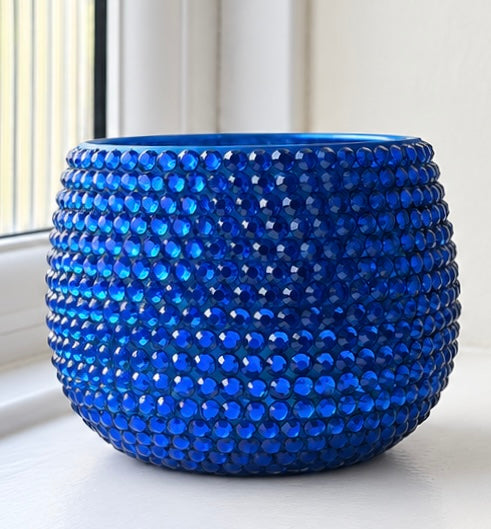 Blue ceramic plant pot covered in a sparkling blue crystals shown against a blurred white background. 