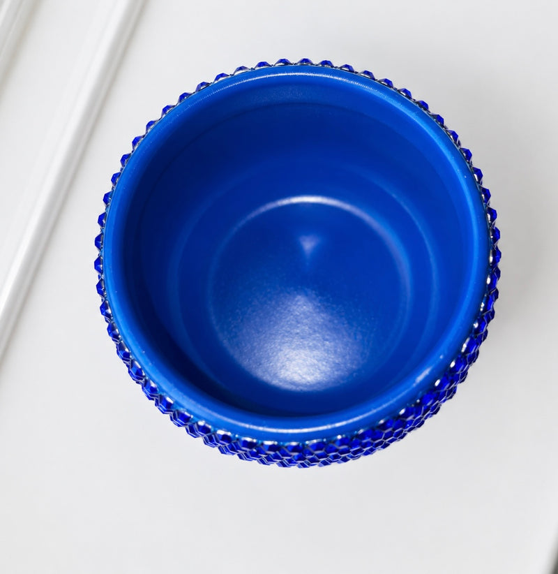 A top-down view of a vibrant cobalt blue ceramic plant pot with a textured, beaded outer rim, set against a clean white background.