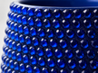 Close-up of a dark blue ceramic plant pot covered in cobalt blue crystals, showing the glossy reflective surfaces against a light neutral background.