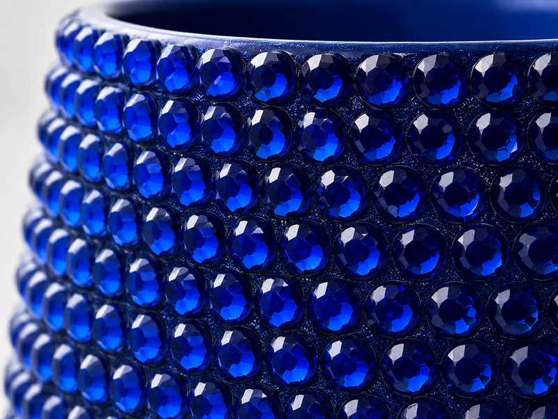 Close-up of a dark blue ceramic plant pot covered in cobalt blue crystals, showing the glossy reflective surfaces against a light neutral background.