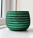 A round green ceramic plant pot with a textured, horizontal pattern and decorated with dark green and light green crystals, sitting on a white windowsill