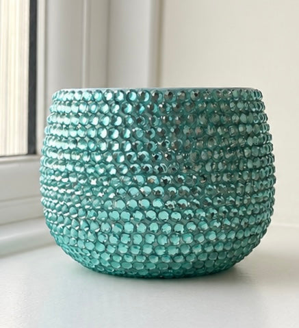A round jade planter covered in small faceted crystals, sitting on a white windowsill with a window and wall visible in the background.