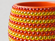Close-up of a ceramic plant pot decorated  with rows of faceted translucent crystals in orange and yellow with a solid orange interior visible at the top.
