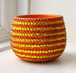 A small round ceramic planter pot decorated with horizontal stripes of faceted orange and yellow crystals, set on a white surface near a window.