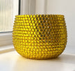 A round, textured yellow planter decorated with sparkling yellow crystals  sitting on a windowsill with natural light.