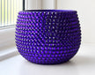 A round, deep purple ceramic planter pot covered in a textured, beaded pattern of faceted purple crystals, sitting on a white windowsill.