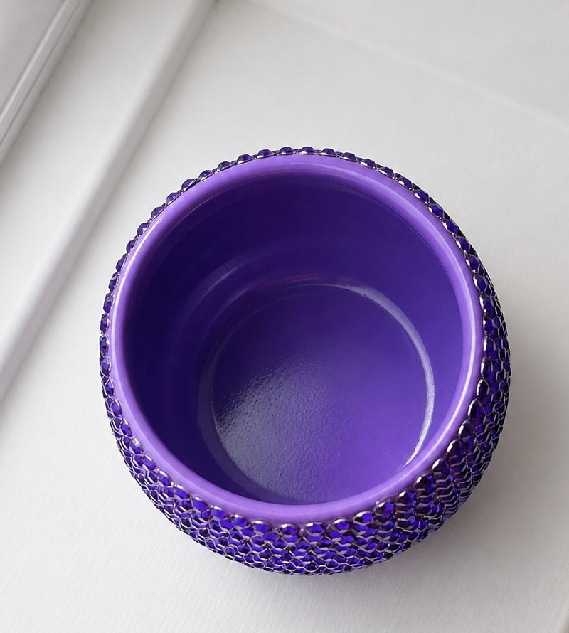 A purple ceramic plant pot with a textured, beaded outer rim, photographed from a top-down angle on a white surface.