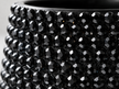Close-up of a glossy black faceted gemstone-covered ceramic plant pot,, showing rows of round black crystals on a dark base.