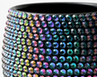 A close-up of shot a black iridescent  cylindrical plant pot covered in rows of faceted iridescent crystals that shift between blue, green, purple, and gold.