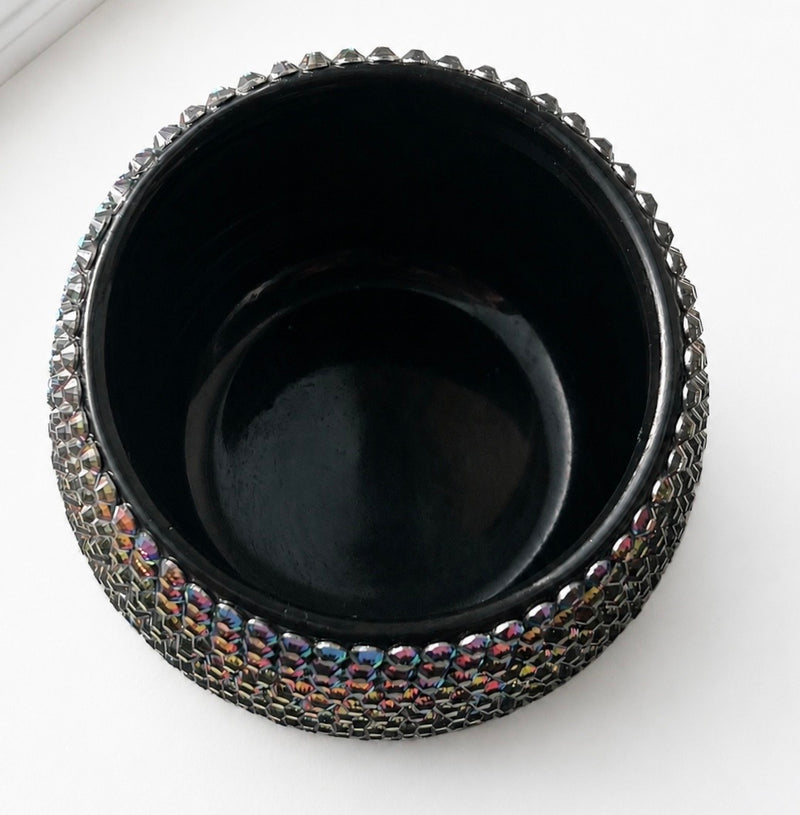 A black ceramic plant with a textured, beaded metallic rim that reflects iridescent rainbow colors, shown from a top-down perspective on a white background.