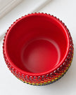 A red ceramic plant pot with a textured, beaded outer rim and a multicolor patterned band near the base, shown from a top-down perspective on a white surface.