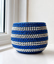 A small round decorative planter covered in horizontal stripes of faceted blue and silver crystals, sitting on a windowsill.