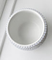 A white ceramic bowl with a textured, beaded outer rim, photographed from a top-down angle on a clean white surface.