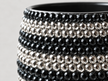 Close-up of a ceramic plant pot decorated with multiple horizontal rows of faceted crystals in black and silver, set against a light gray background.