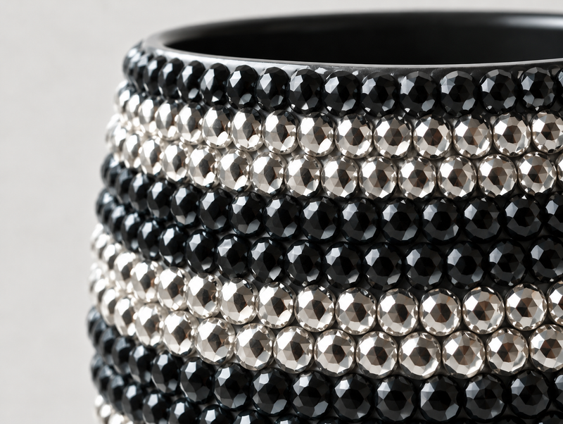 Close-up of a ceramic plant pot decorated with multiple horizontal rows of faceted crystals in black and silver, set against a light gray background.