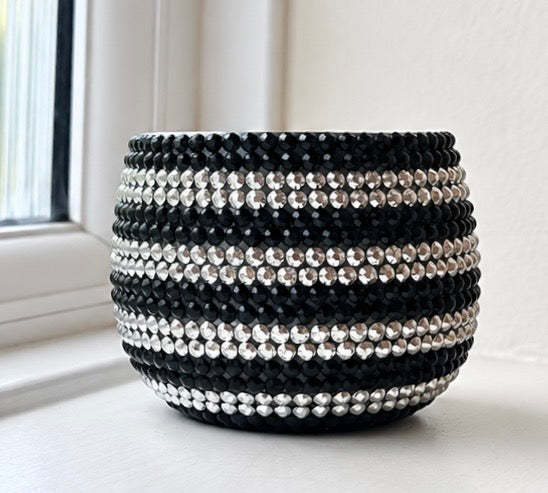 A round black and silver planter decorated with horizontal rows of faceted black and silver crystals, set on a windowsill.