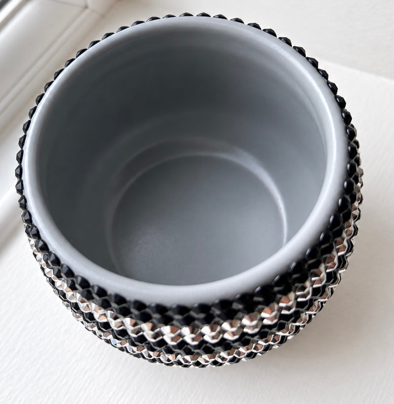 A small round ceramic plant pot with a matte gray interior and a black-and-silver textured exterior, shown from a top-down angle on a white surface.